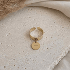 Une bague en acier inoxydable est posée sur une table en travertin, il y a une pampille "mom", bijou de maternité