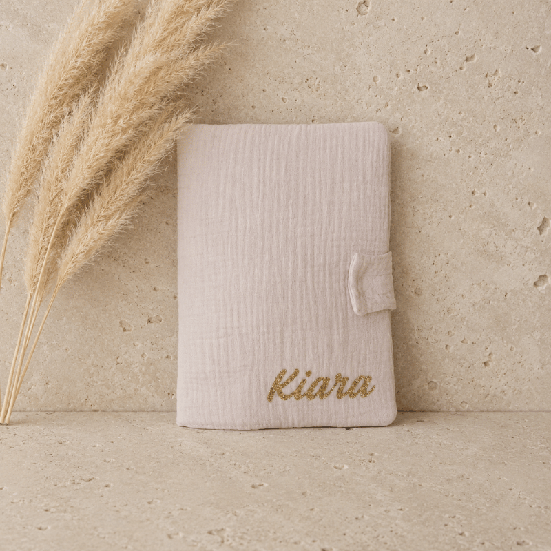 protège carnet de santé en gaze de coton beige, un prénom de bébé est écrit en doré.