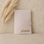 protège carnet de santé en gaze de coton beige, un prénom de bébé est écrit en doré.