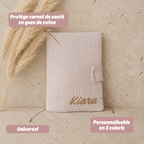 protège carnet de santé en gaze de coton beige posé sur une table en travertin. Cadeau de bébé