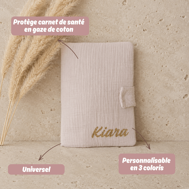 protège carnet de santé en gaze de coton beige posé sur une table en travertin. Cadeau de bébé