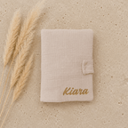protège carnet de santé en gaze de coton beige, un prénom de bébé est écrit en doré.